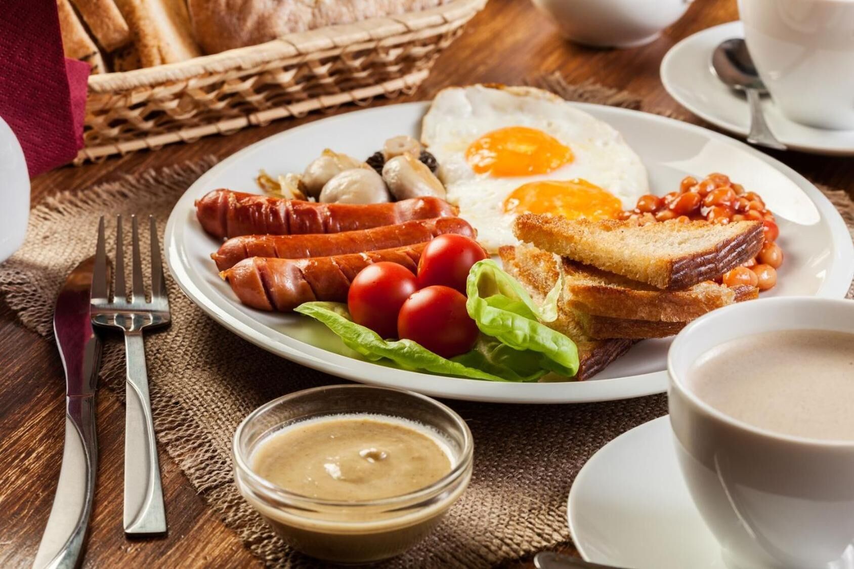 Une assiette de petit-déjeuner comprenant des saucisses, des tomates, de la laitue, des œufs au plat, des toasts et des haricots.