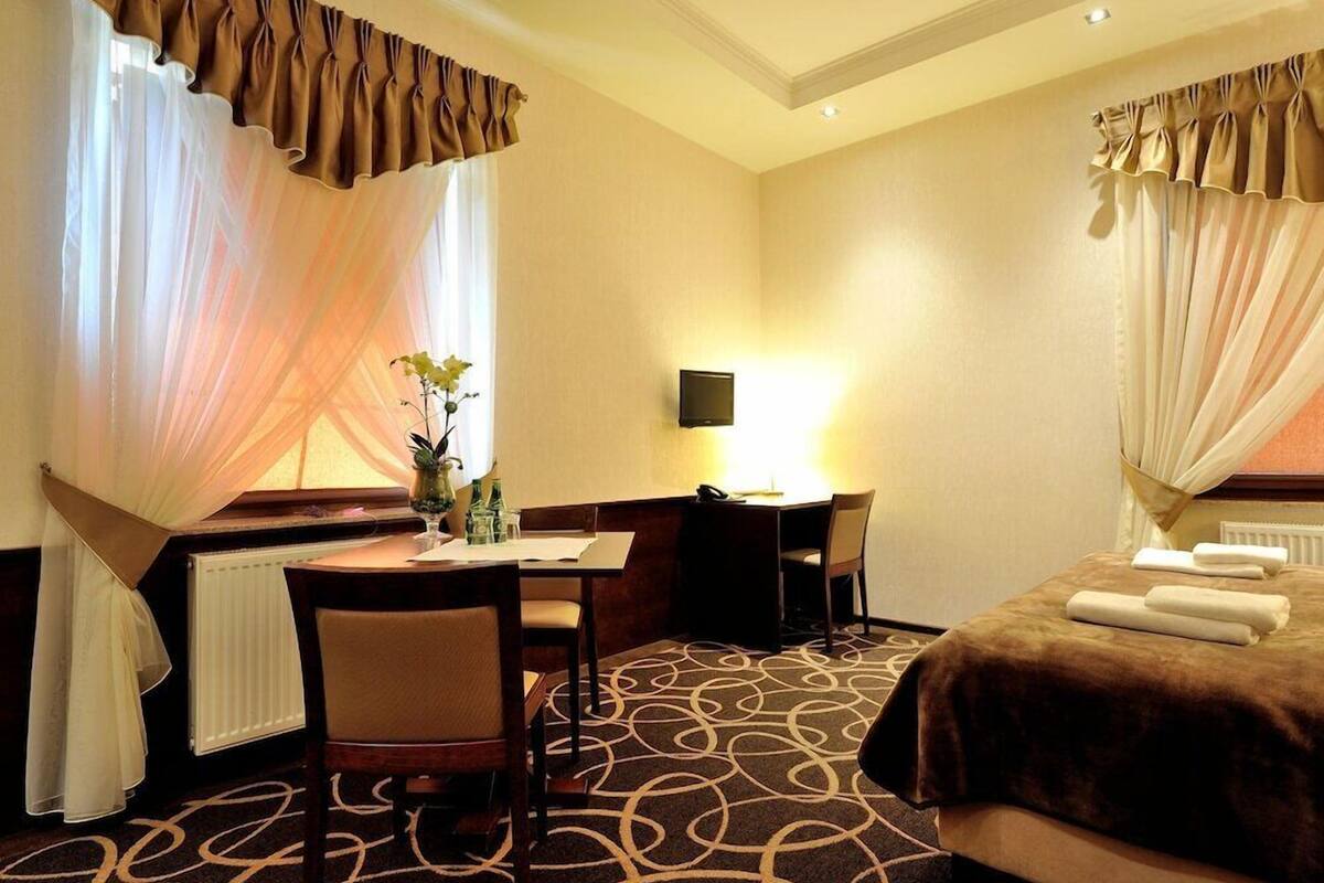 A hotel room with a bed, a desk, a chair, a television, and a window with curtains.
