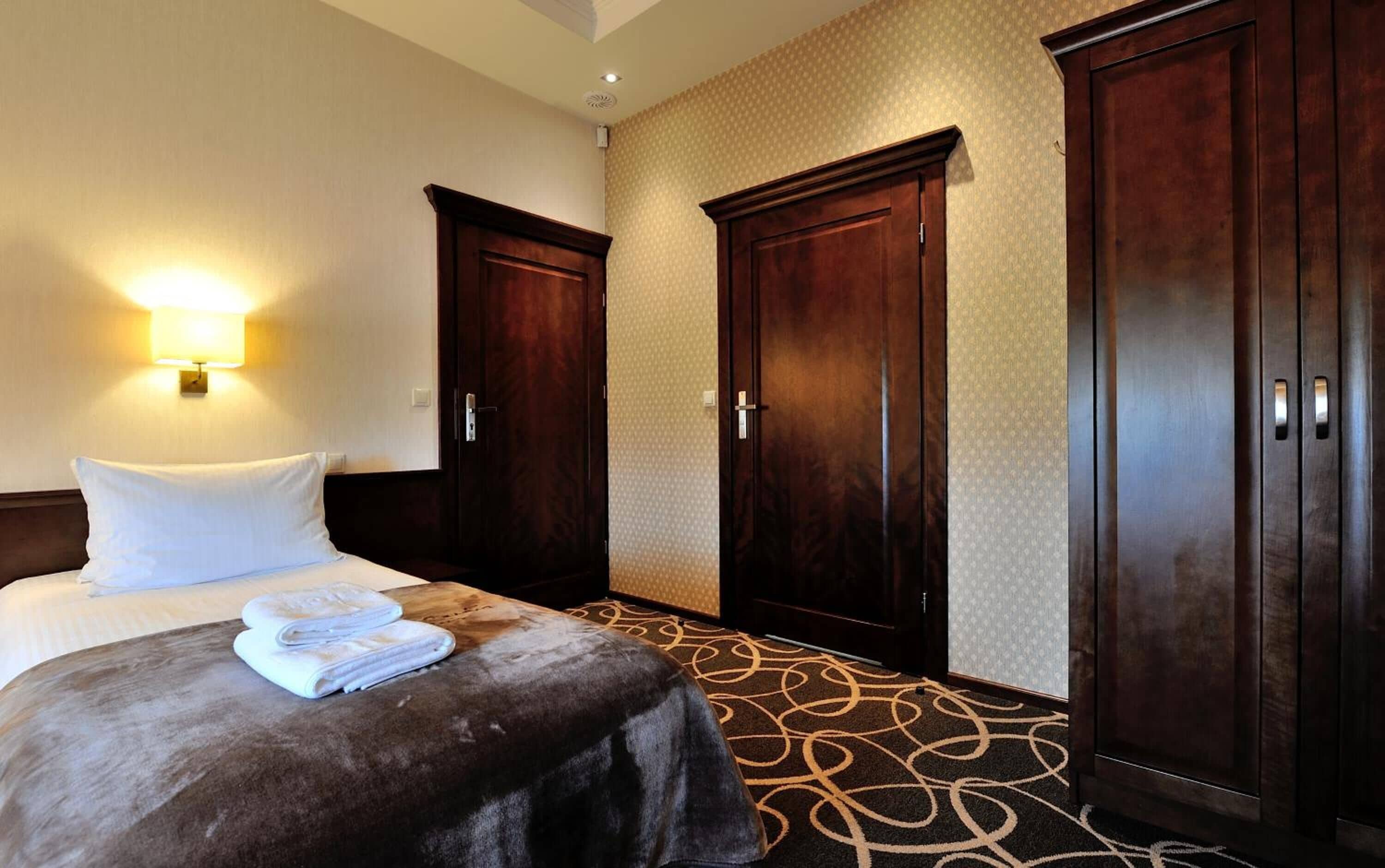 A hotel room with a bed, two wardrobes, a wall-mounted lamp, and a patterned carpet.