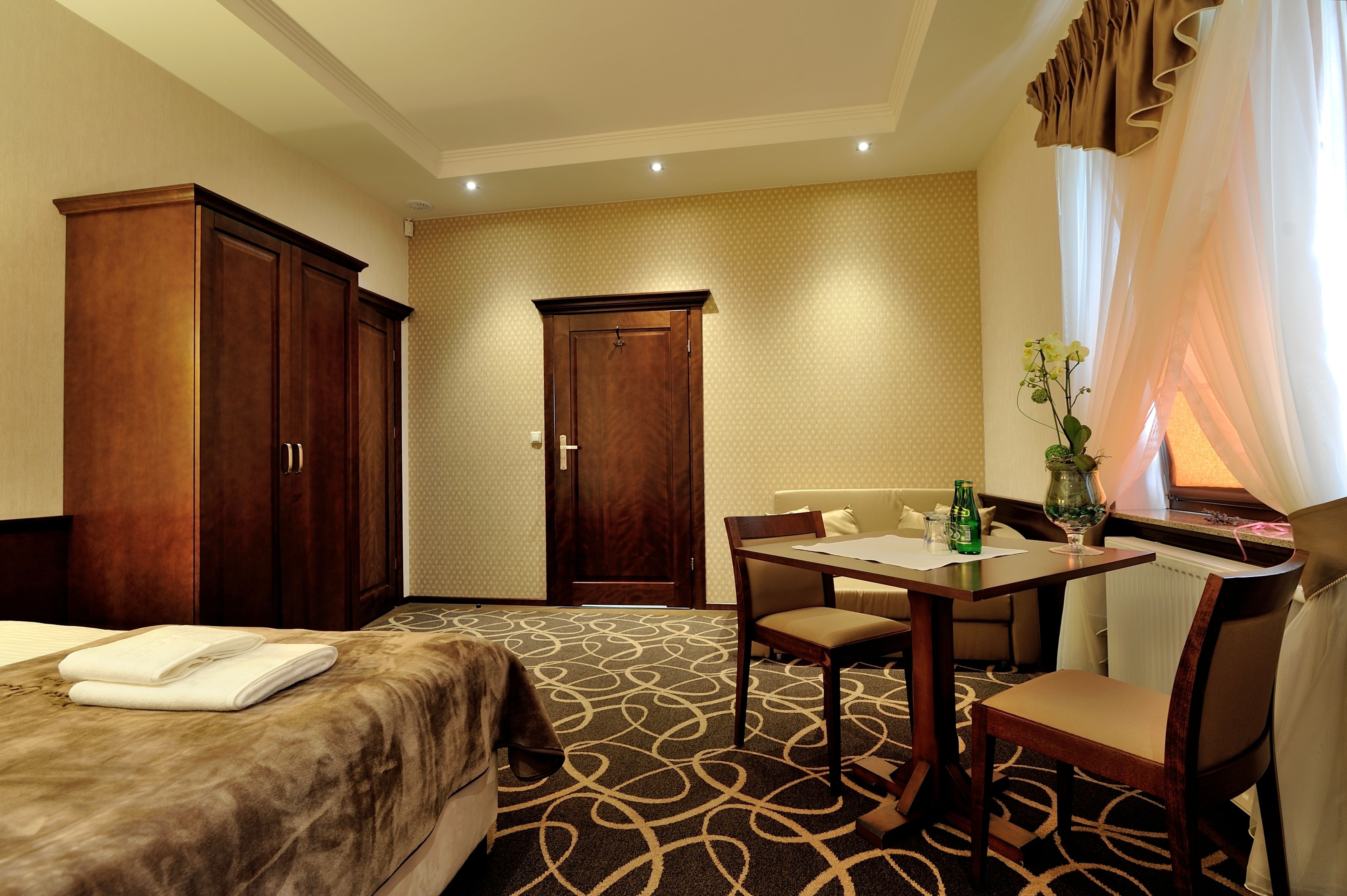 A hotel room with a bed, a desk with a chair, a wardrobe, and a door.