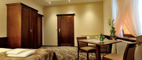 A hotel room with a bed, a desk with a chair, a wardrobe, and a door.