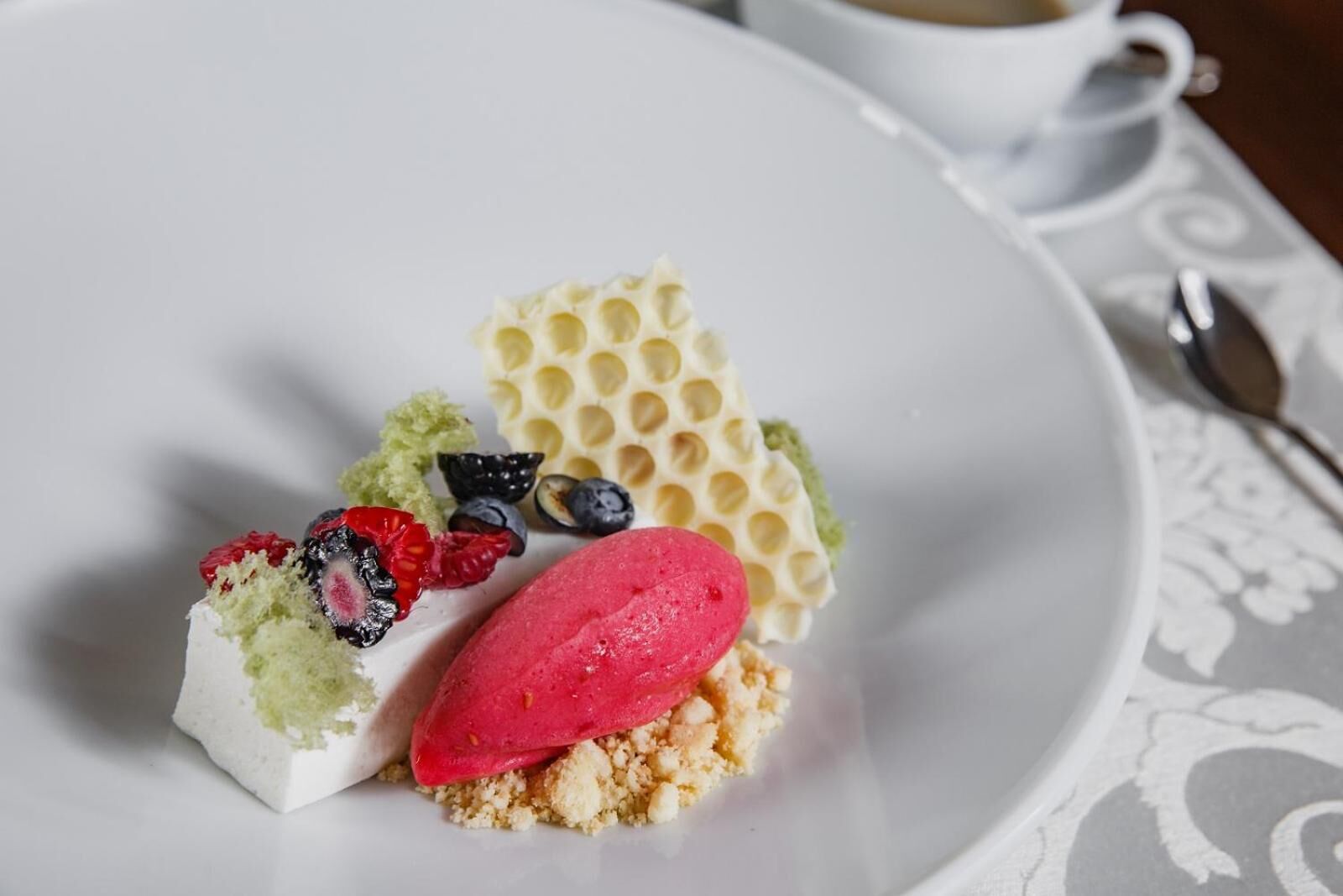 Ein Dessertteller mit Kuchenstück, einer Kugel Eis und einer honigwabenartigen Süßigkeit, dazu eine Tasse Kaffee.