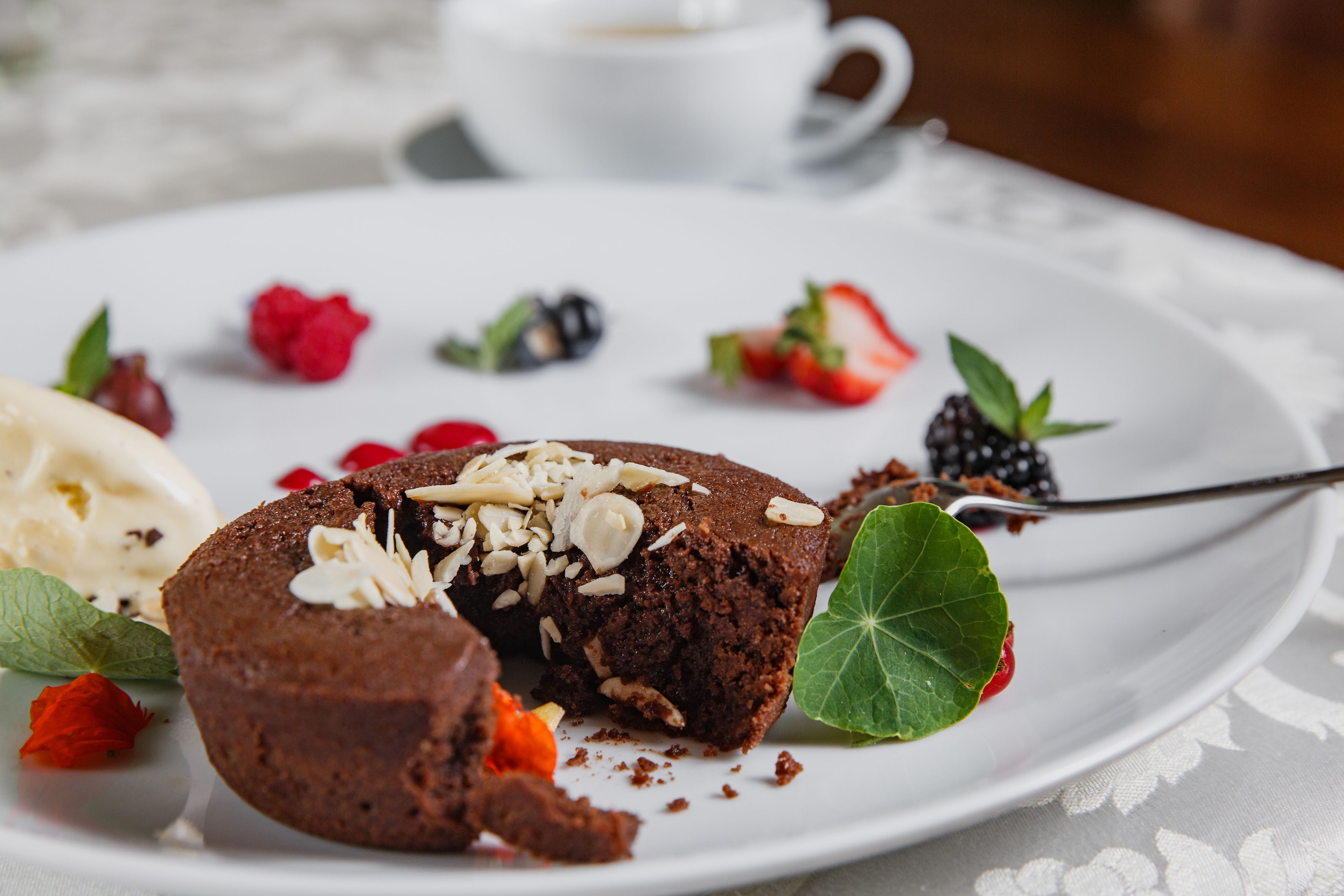 A dessert plate with a chocolate lava cake, strawberries, raspberries, and a cup of coffee.