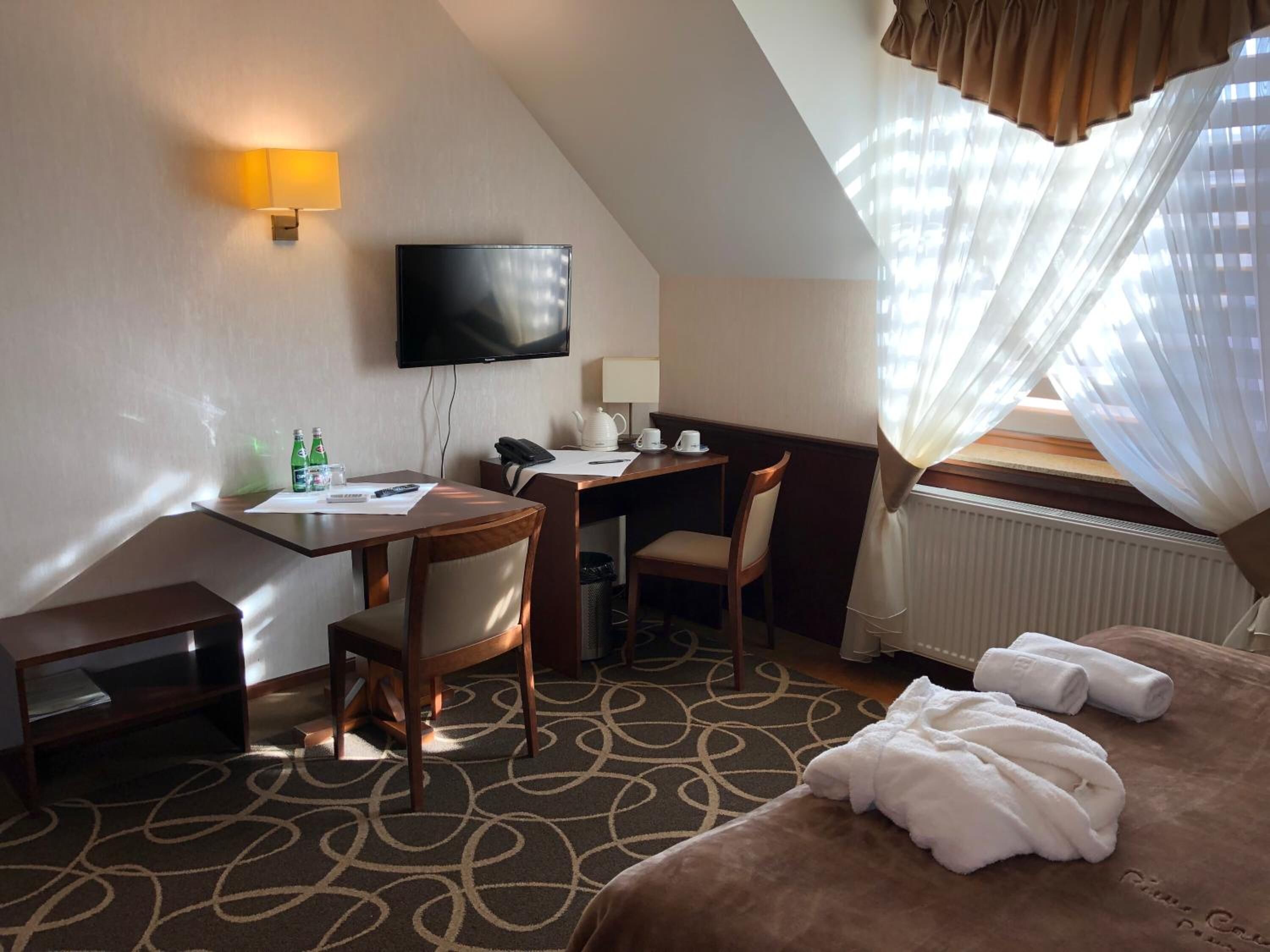 Quarto de hotel com escrivaninha, cadeira, cama e televisão na parede.