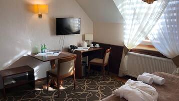 Quarto de hotel com escrivaninha, cadeira, cama e televisão na parede.