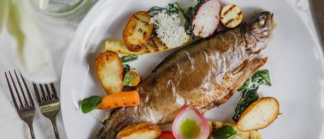 A plate with grilled fish, potatoes, carrots, radishes, and cherry tomatoes.