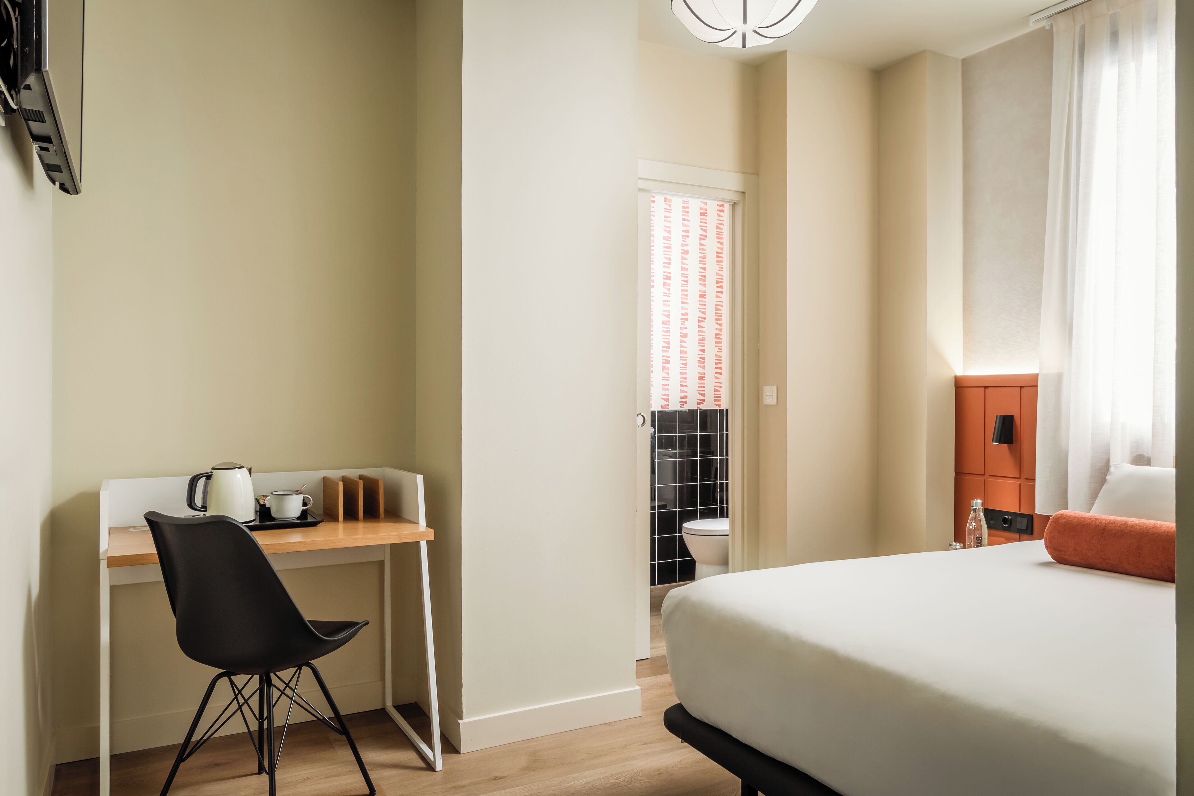 A hotel room with a bed, a desk with a chair, a kettle, and a small table.