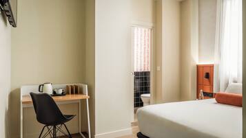 A hotel room with a bed, a desk with a chair, a kettle, and a small table.