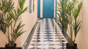 A hallway with a checkered floor, potted plants, and a blue door at the end. - BYPILLOW Amari (Bilbao)