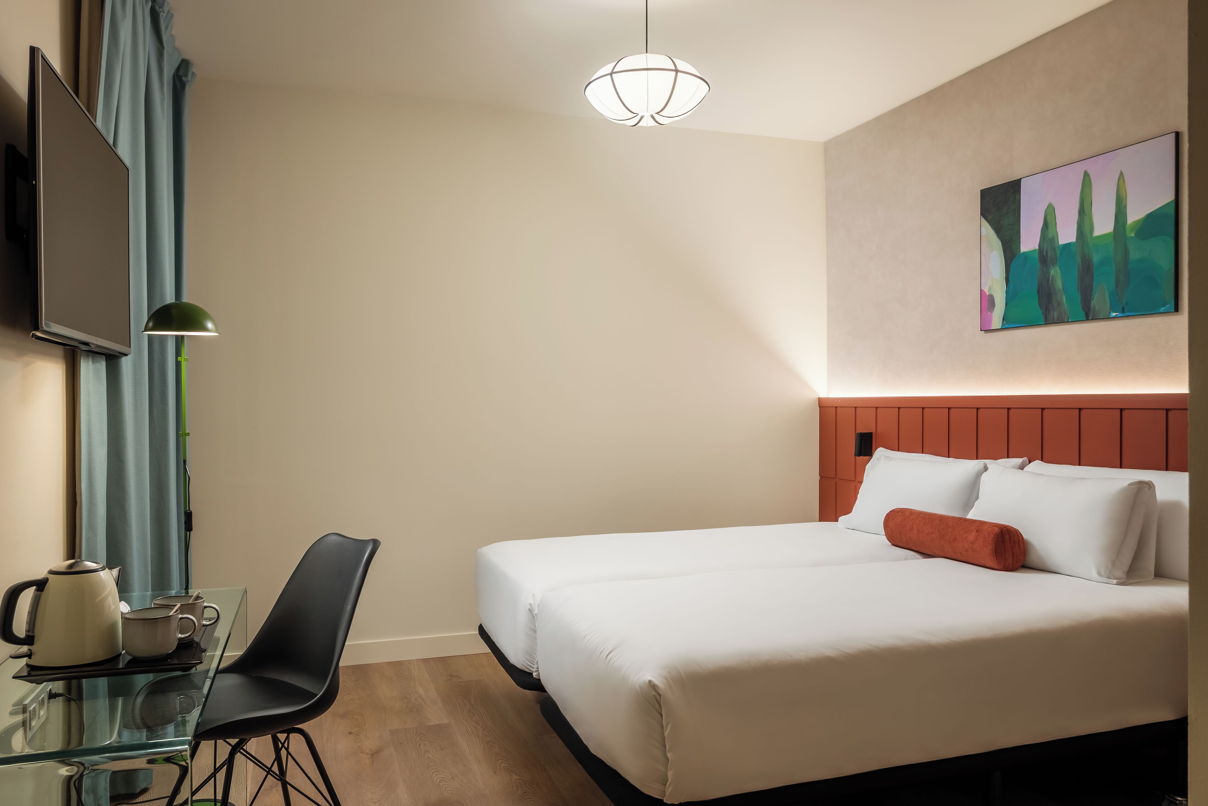 Habitación de hotel con cama, escritorio con silla, televisor y un cuadro en la pared.