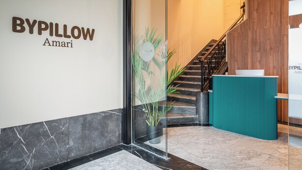 A reception area with a glass door, a staircase, and a teal reception desk. - BYPILLOW Amari (Bilbao)