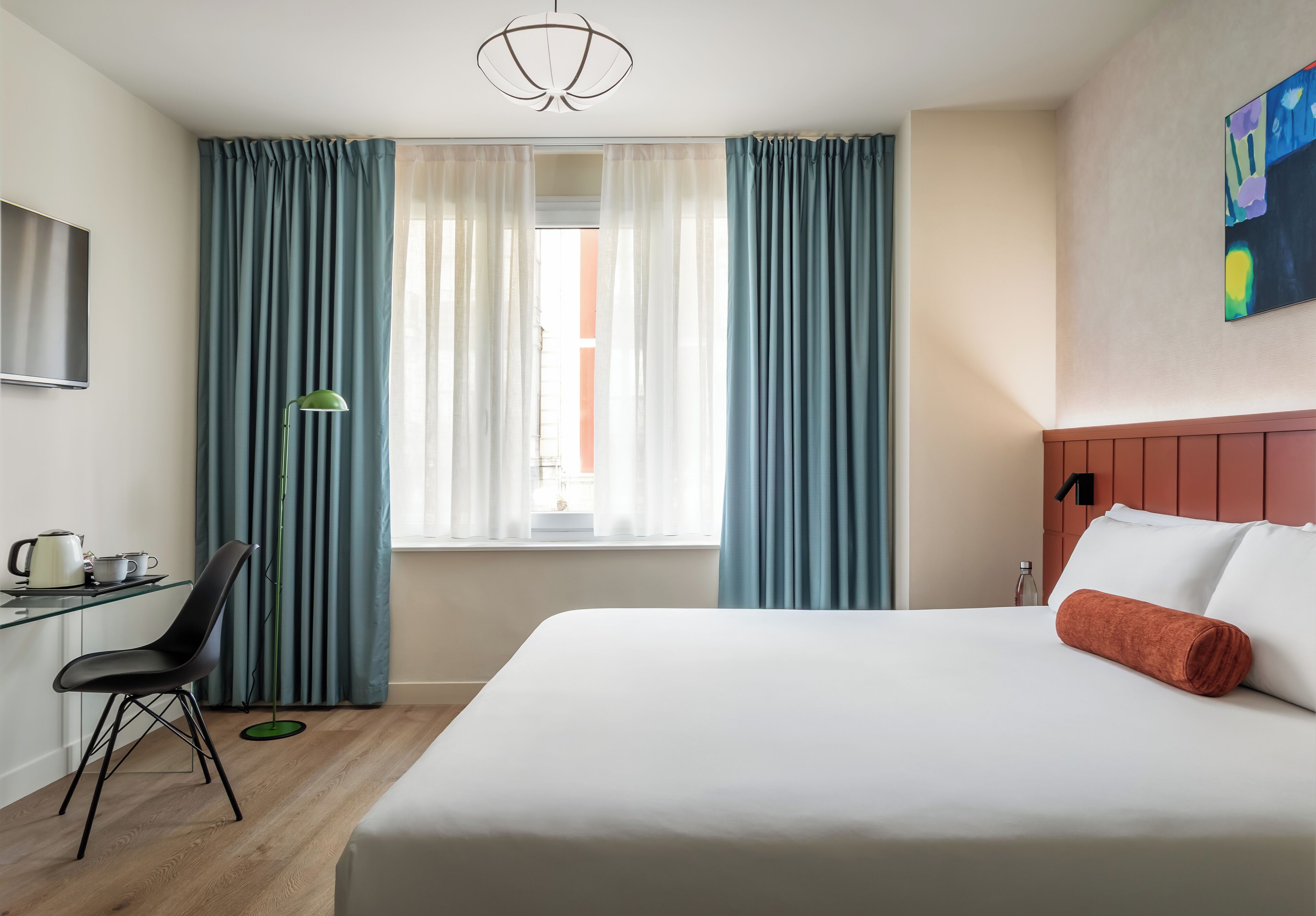 Una habitación de hotel con cama, escritorio con silla, televisión y cortinas.