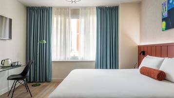 Una habitación de hotel con cama, escritorio con silla, televisión y cortinas.