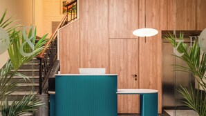 A modern reception area with a wooden wall, a staircase, and a teal-colored reception desk. - BYPILLOW Amari (Bilbao)