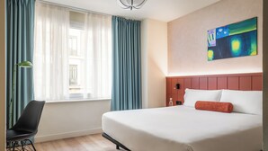 A hotel room with a bed, a chair, a window with curtains, and a painting on the wall. - BYPILLOW Amari (Bilbao)