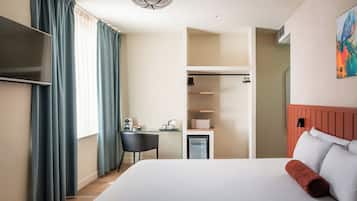 A hotel room with a bed, a desk with a chair, a TV, and a mini-fridge.
