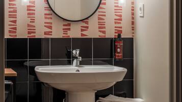 Un baño con un lavabo blanco, baldosas negras, un espejo y dos luces empotradas.