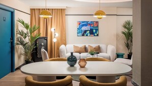 A modern dining area with a round table, two yellow pendant lights, a white sofa with brown cushions, and a painting on the wall. - BYPILLOW Amari (Bilbao)