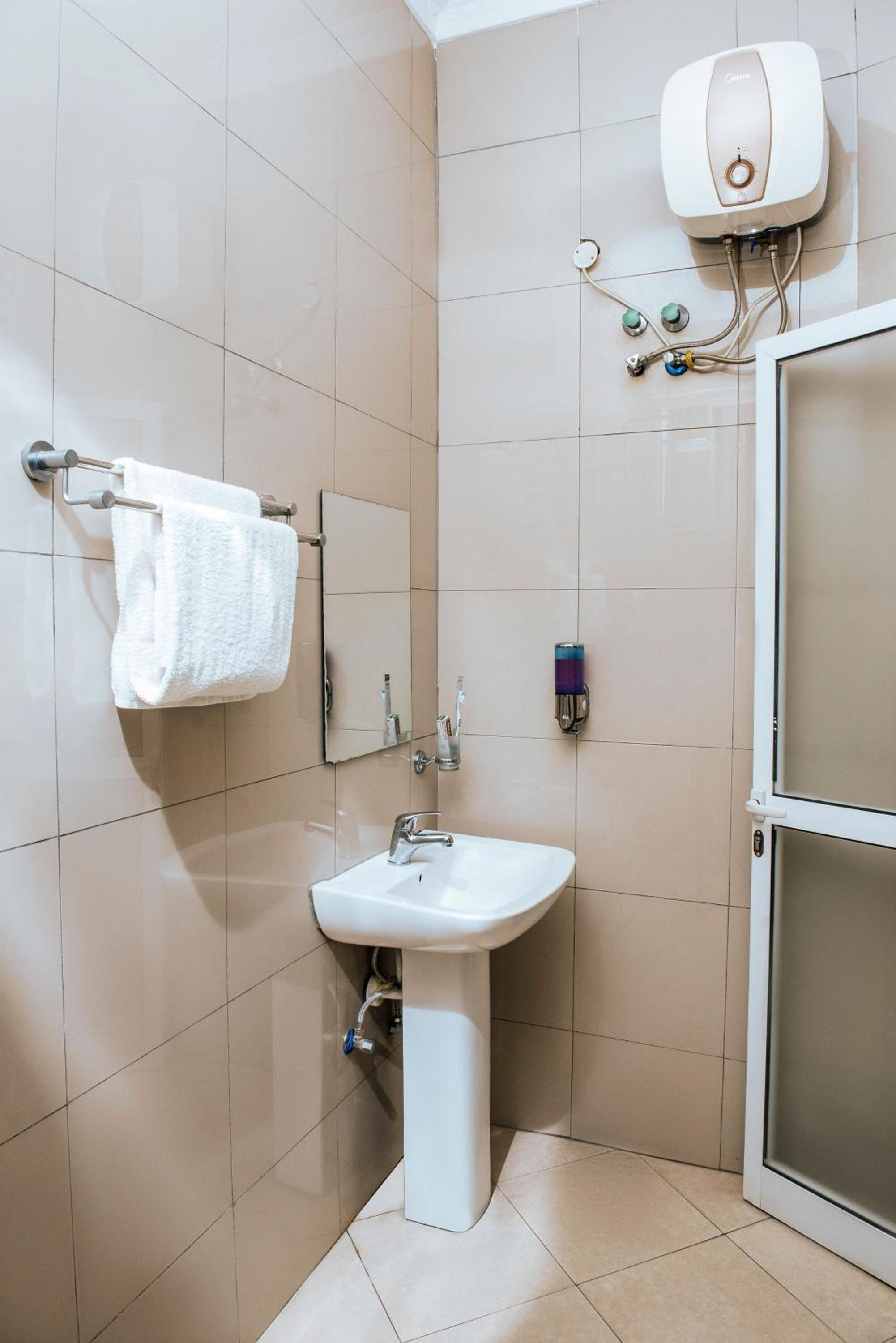 Un bany amb un lavabo blanc, un penjador de tovalloles, un mirall i una cabina de dutxa.