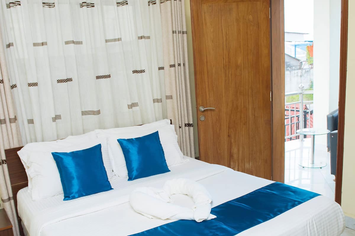 A neatly made bed with blue and white bedding, a wooden door, and a view of the outside balcony.