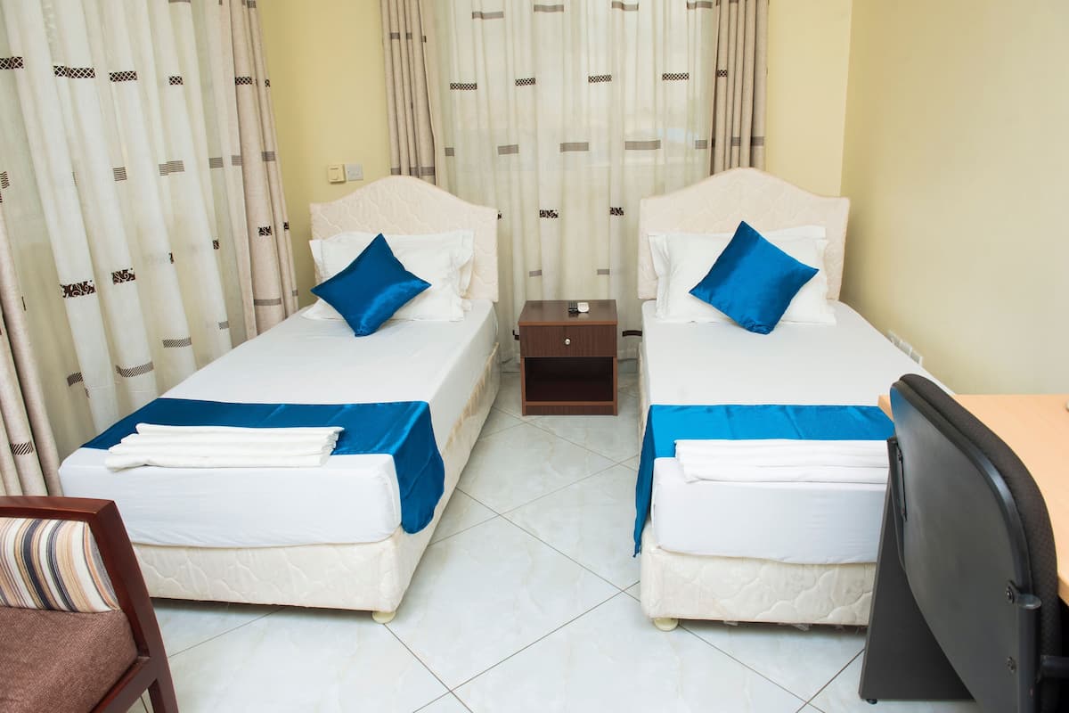 A hotel room with two beds, each with a blue bedspread and pillows, a small wooden nightstand, a chair, and a television.
