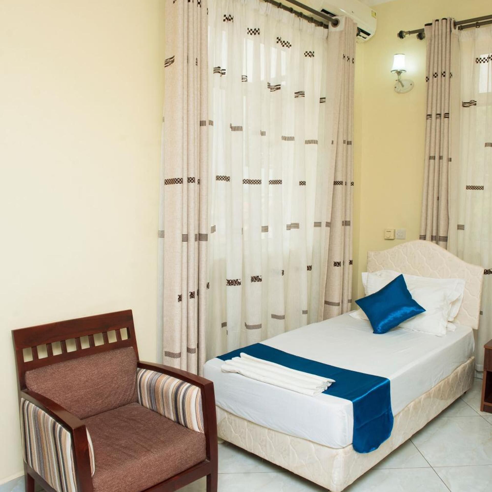 A hotel room with a bed, a chair, and curtains.