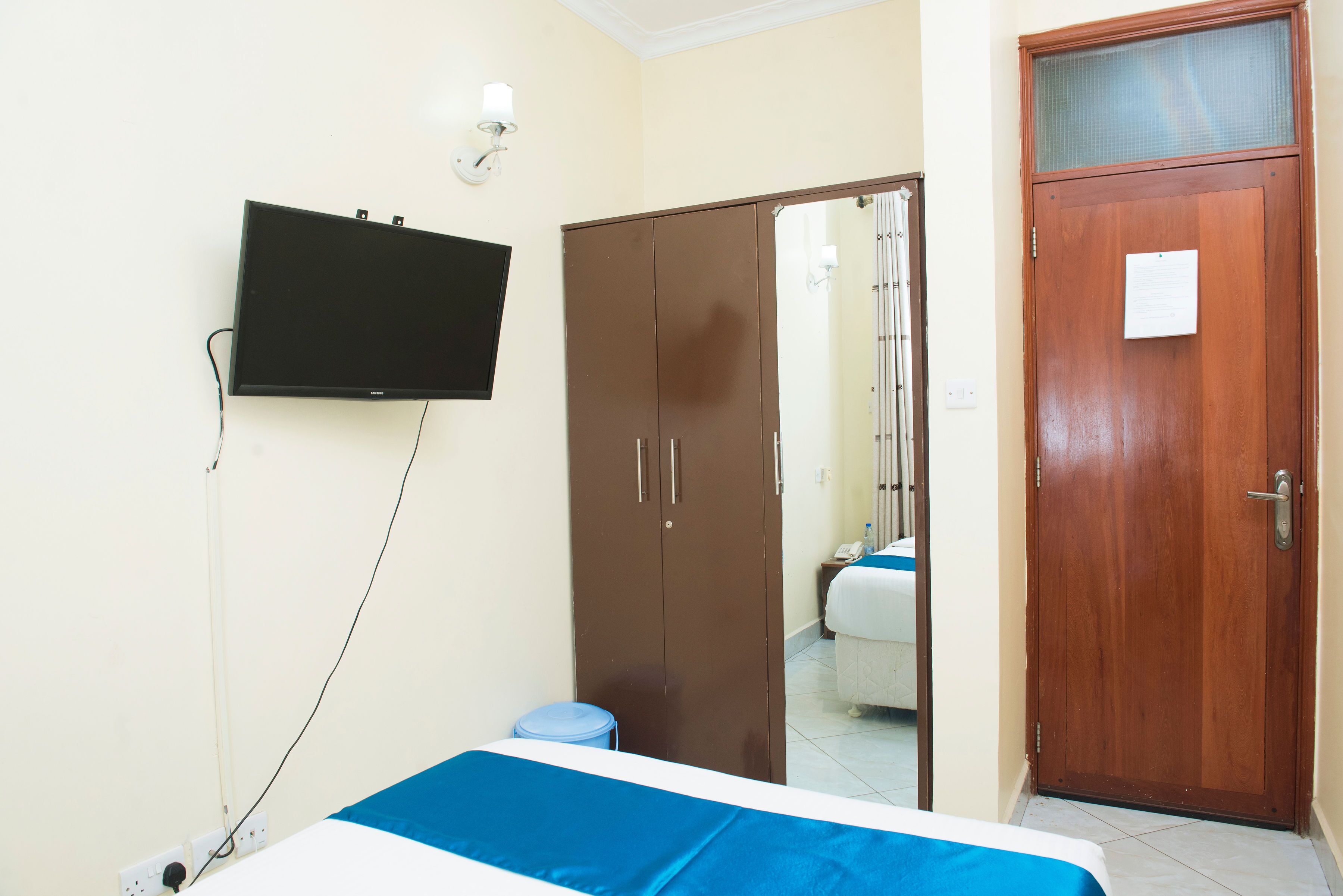 A hotel room with a bed, a wardrobe, a television mounted on the wall, and a door with a note on it.