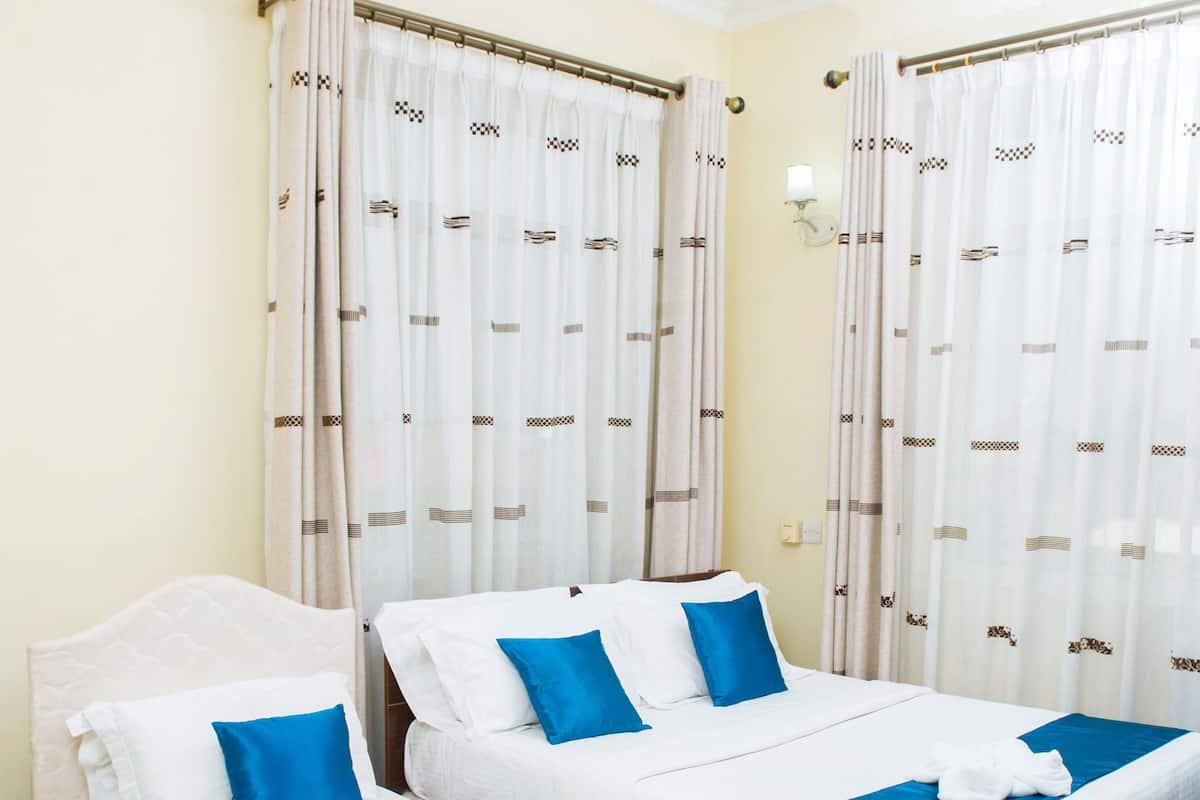 A hotel room with two beds, beige walls, white curtains with brown patterns, and a ceiling fan.