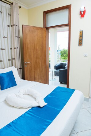 Une chambre d’hôtel avec un lit, une couvre-lit bleue, un oreiller blanc, un coussin de nuque blanc, une porte en bois et un balcon avec une chaise.