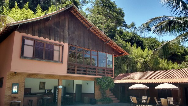 A two-story wooden building with a swimming pool, outdoor seating, and a view of the surrounding greenery. - Pousada Nova Gironda (Paty do Alferes)