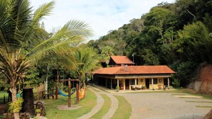 A house with a red roof, surrounded by a gravel driveway and palm trees. - Pousada Nova Gironda (Paty do Alferes)