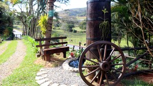 A rustic wooden bench and a large wooden wheel in a garden setting with a stone path and lush greenery. - Pousada Nova Gironda (Paty do Alferes)