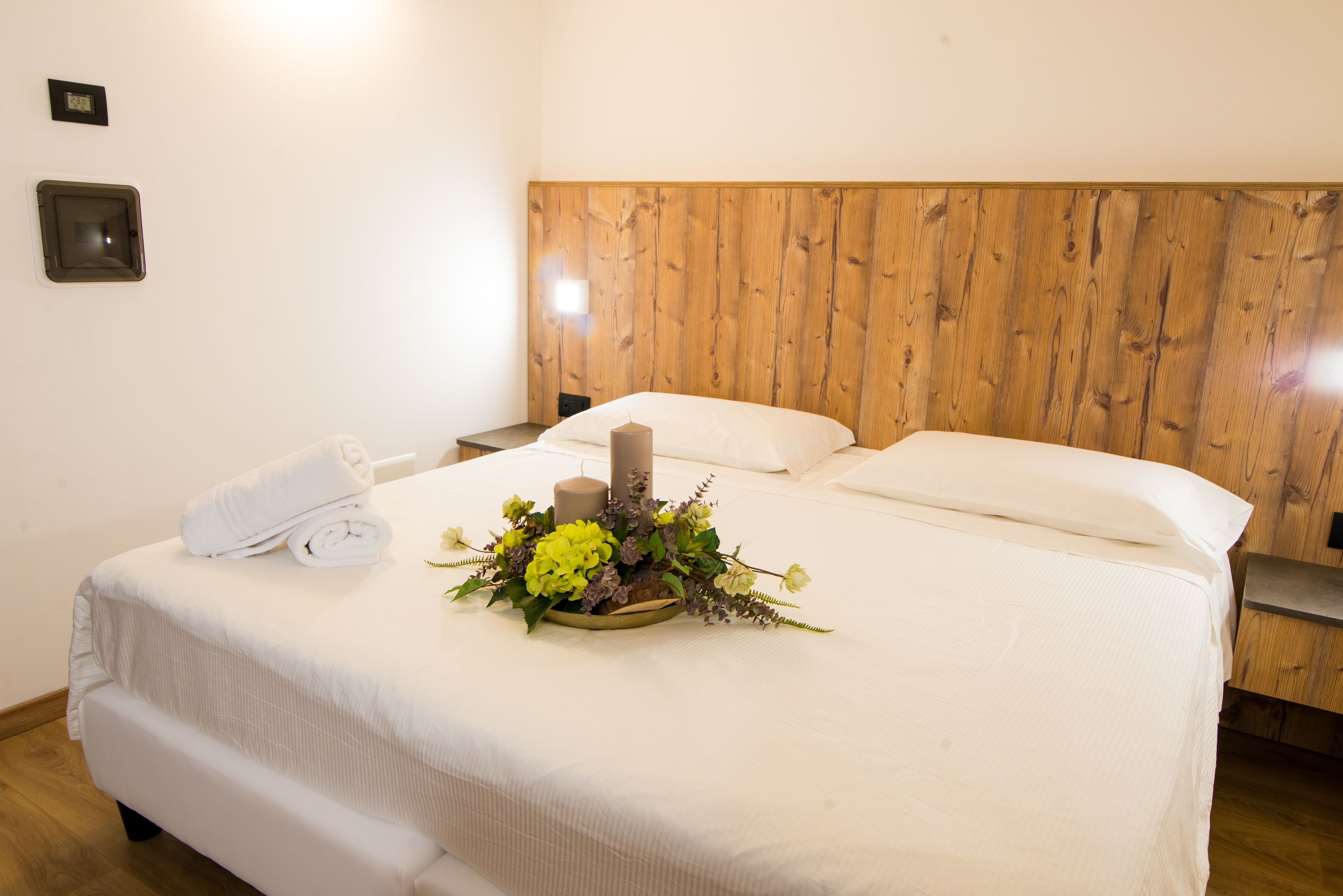 Un letto rifatto con cura, decorato con un centro floreale, un asciugamano bianco e una testiera in legno.