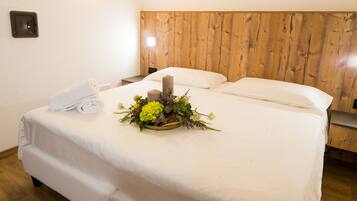 Un letto rifatto con cura, decorato con un centro floreale, un asciugamano bianco e una testiera in legno.