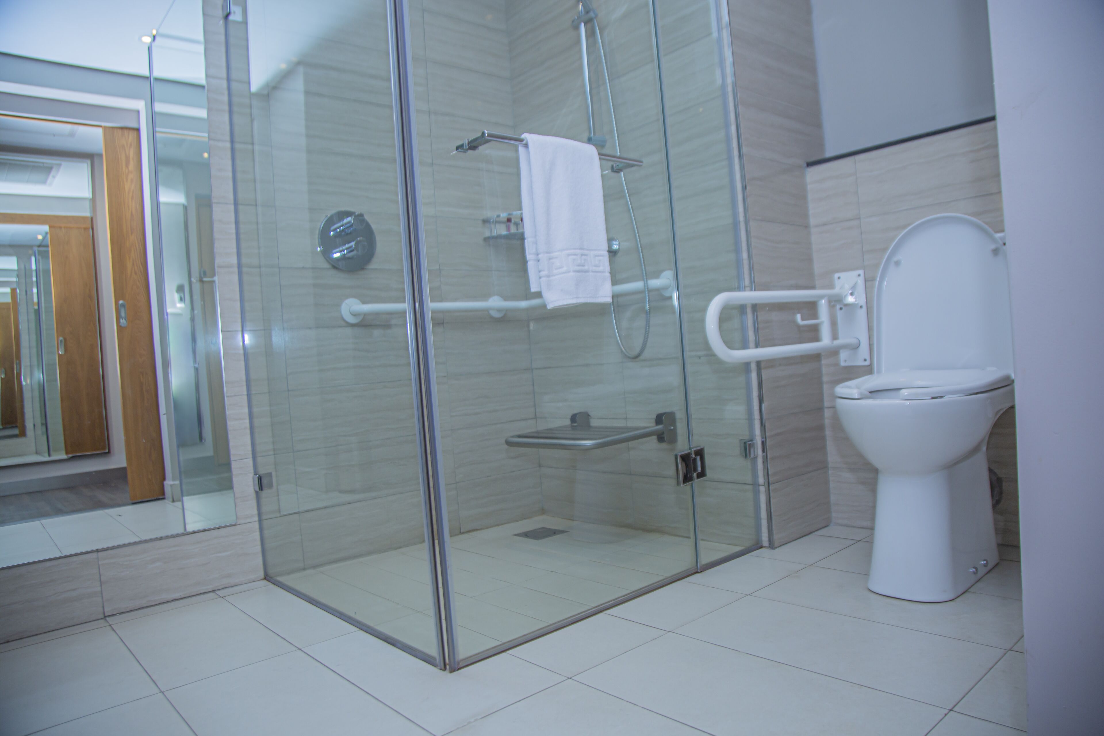 A modern bathroom with a glass-enclosed shower, a white toilet, and a visible handrail.