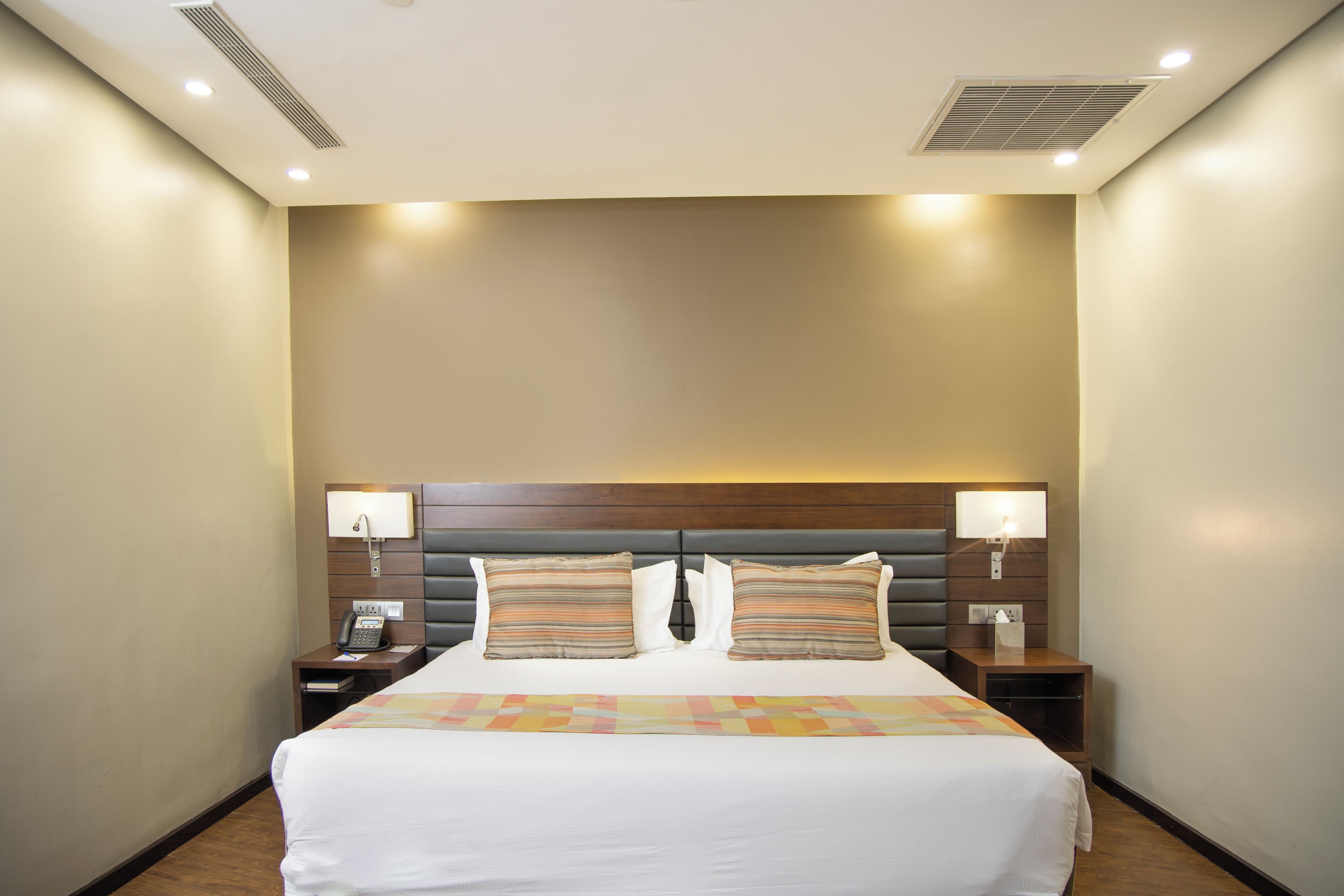 Une chambre d’hôtel avec un grand lit, deux tables de chevet, un téléphone et une tête de lit dotée d’un éclairage intégré.