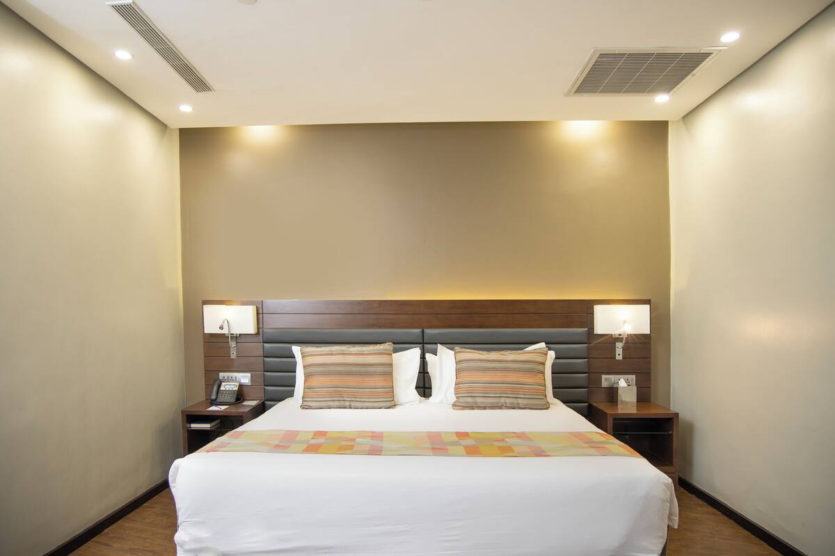 A hotel room with a large bed, two bedside tables, a telephone, and a headboard with built-in lighting.