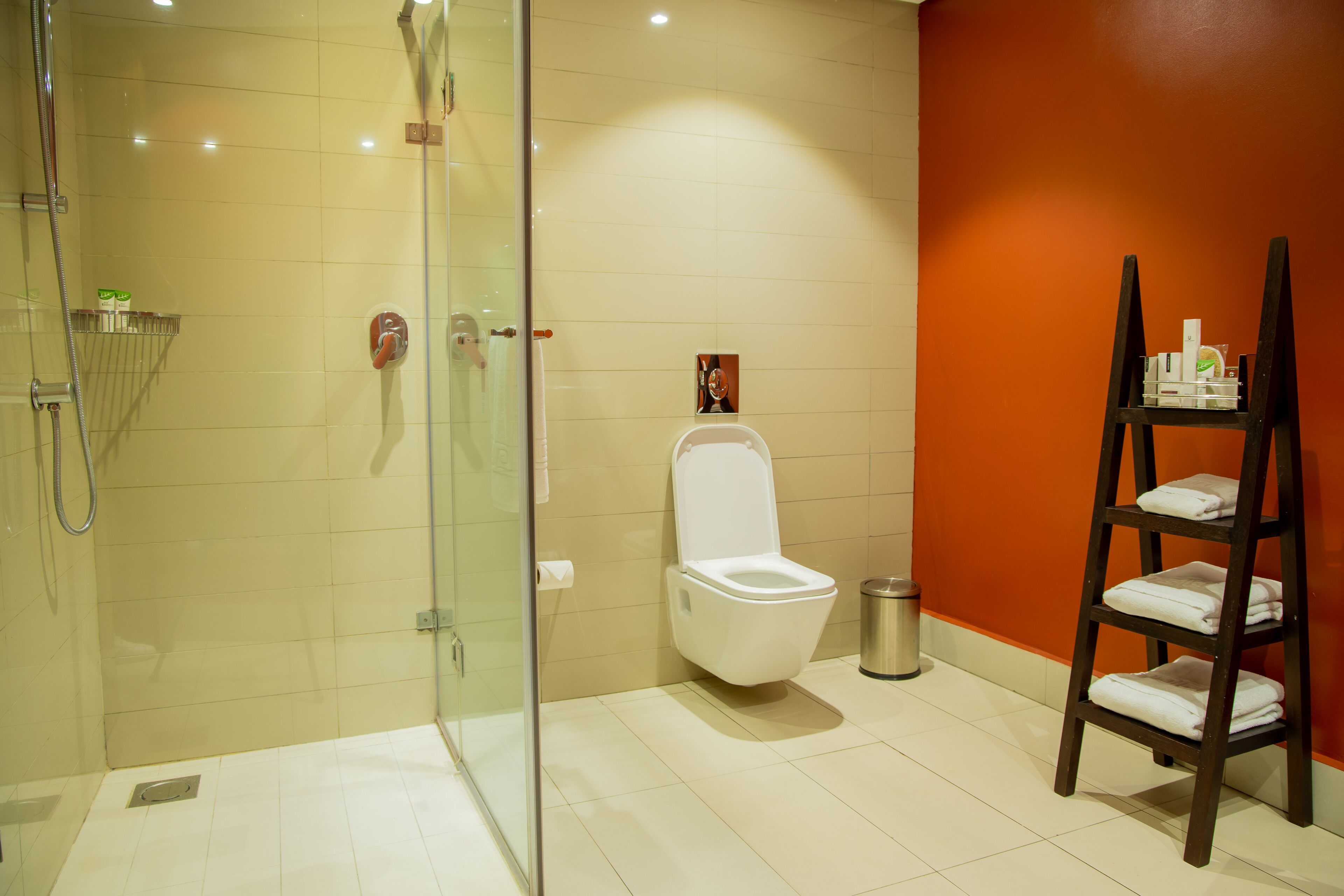 Un baño moderno con cabina de ducha de vidrio, inodoro blanco y estante de madera con toallas.