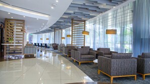 A modern lobby with a reflective floor, patterned sofas, and a large window with sheer curtains. - Ubumwe Grande Hotel (Kigali)