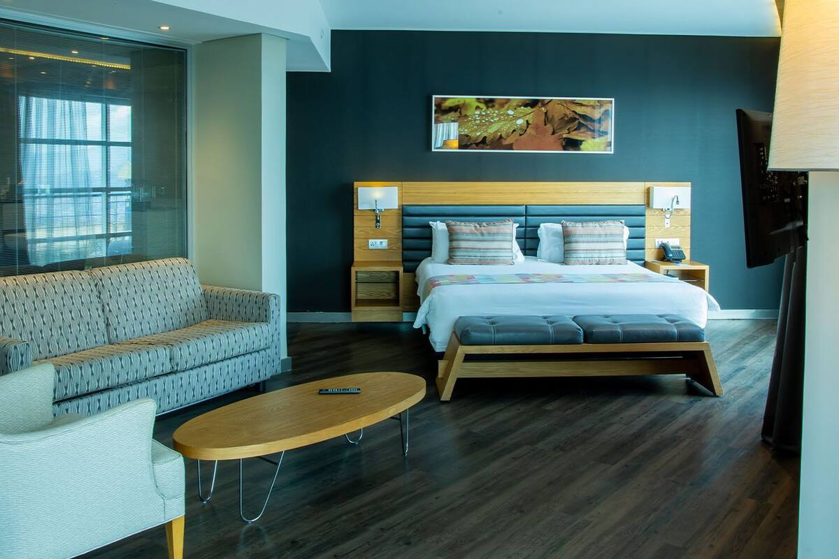 A modern bedroom with a bed, a sofa, a small table, and a window with blinds.