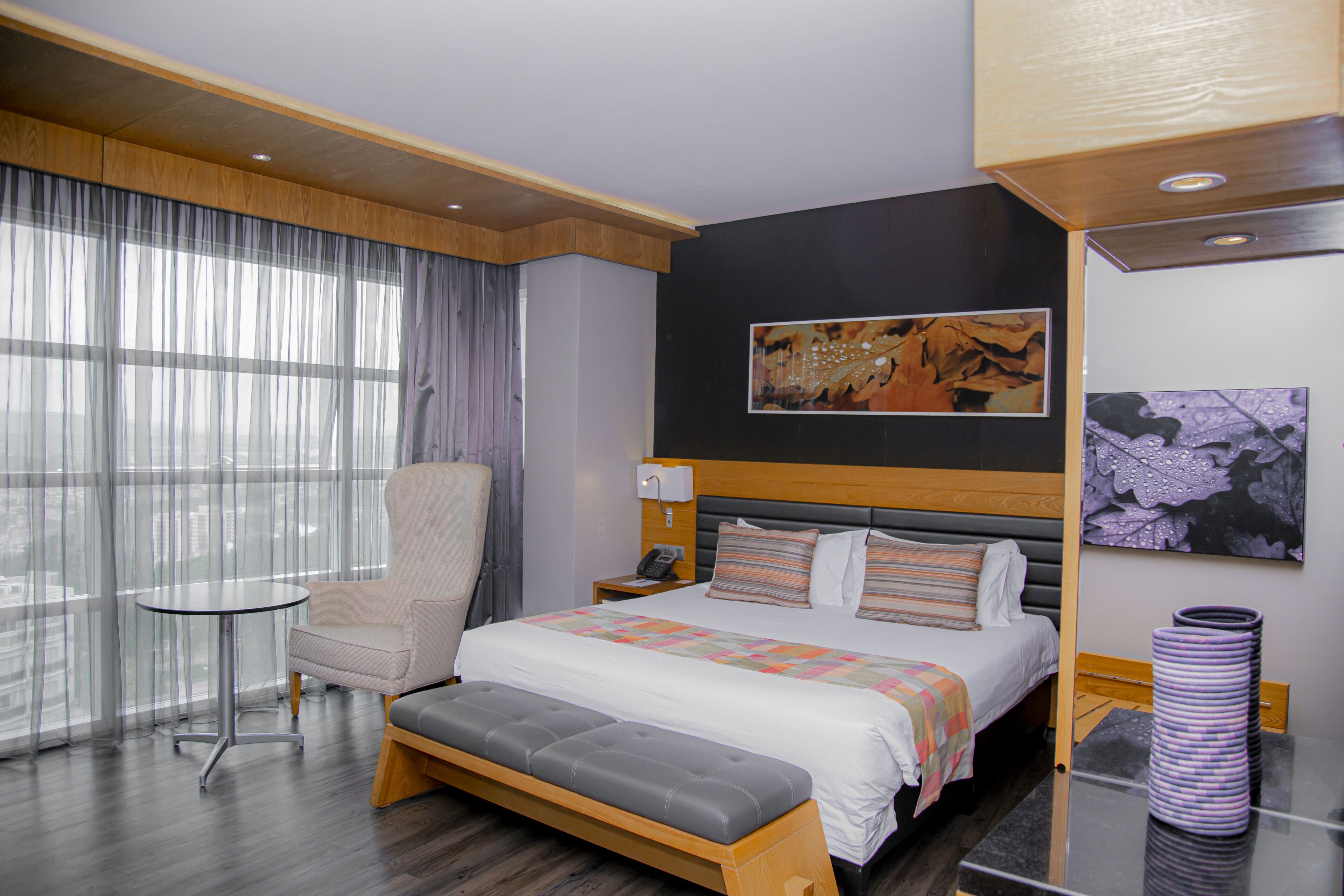 Une chambre d’hôtel moderne avec un grand lit, un coin salon, une petite table et des œuvres d’art accrochées aux murs.