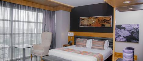 Une chambre d’hôtel moderne avec un grand lit, un coin salon, une petite table et des œuvres d’art accrochées aux murs.