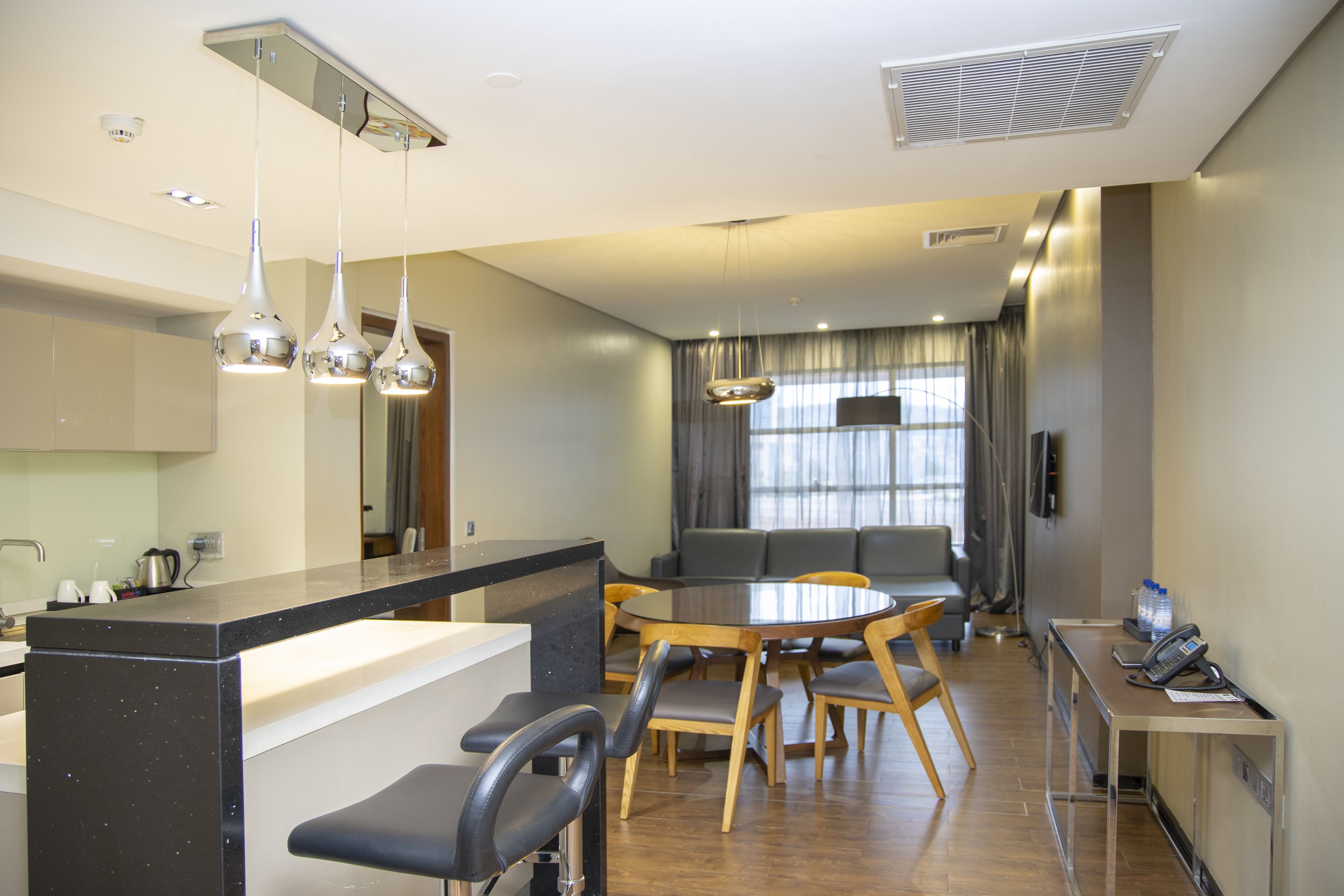 A modern kitchen with a central island, dining area with a round table and chairs, and a seating area with a sofa and curtains.