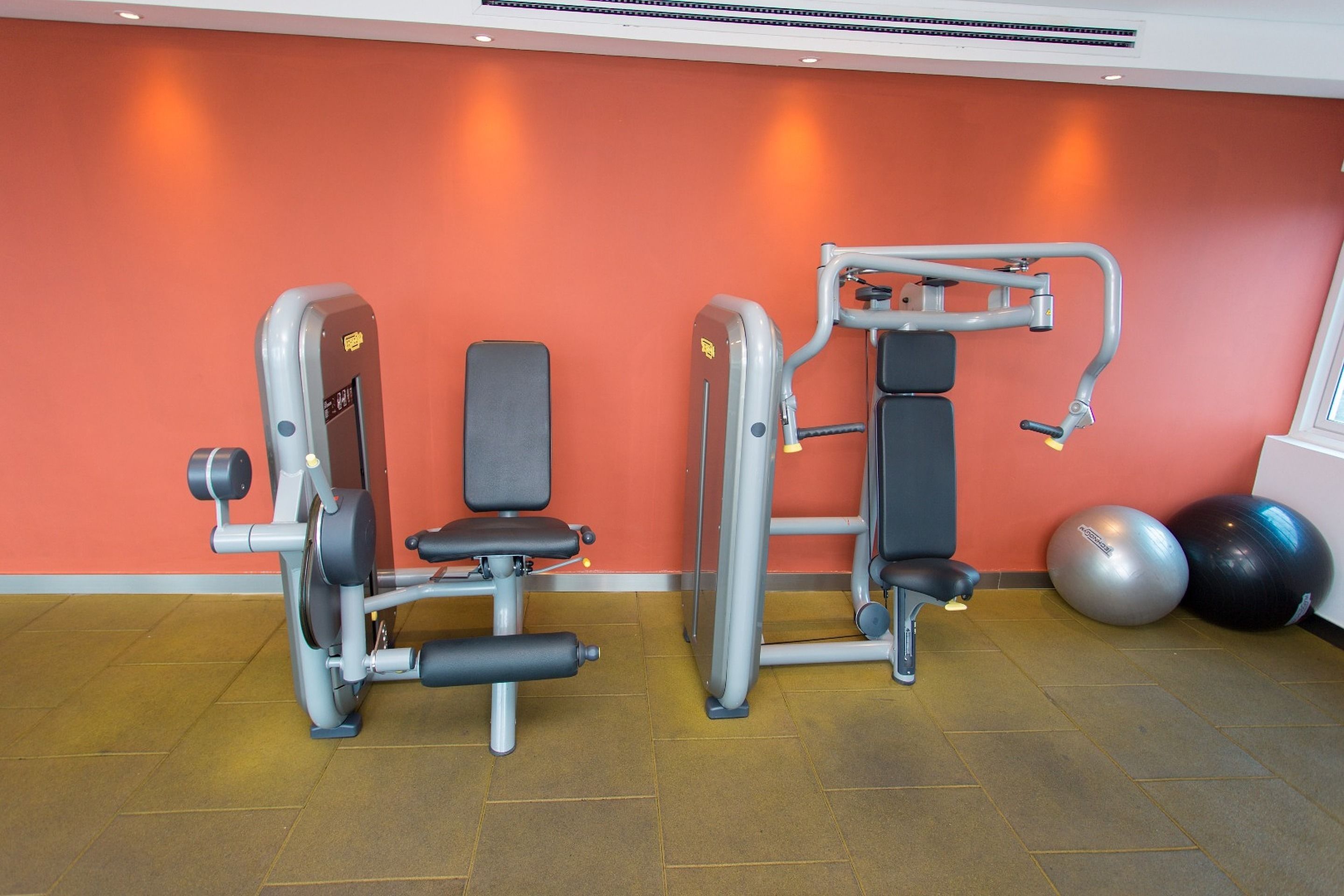 Un gimnasio con dos máquinas de ejercicio, un reloj de pared y dos pelotas de ejercicio.