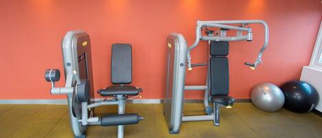 A gym with two exercise machines, a wall clock, and two exercise balls.