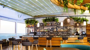 A bar area with wooden stools, a counter with a decorative mural, and hanging plants. - Ubumwe Grande Hotel (Kigali)