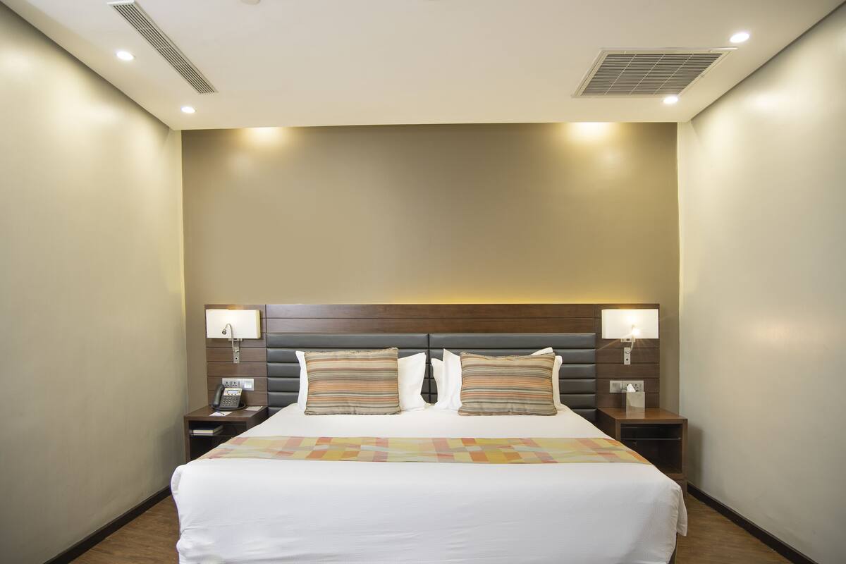 A hotel room with a large bed, two bedside tables, a telephone, and a headboard with built-in lighting.