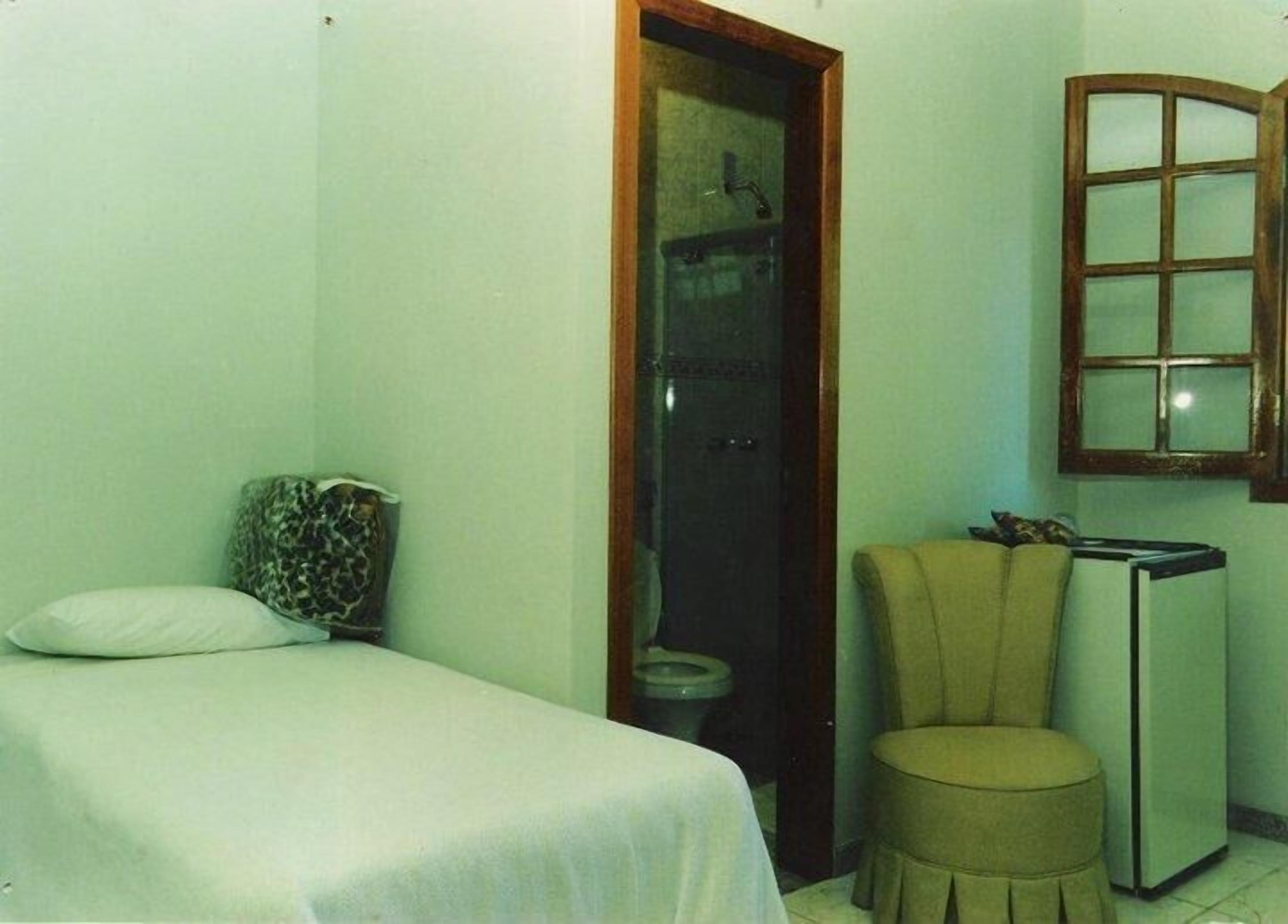 Une petite pièce simple, avec un lit, une chaise, une petite table et une fenêtre.