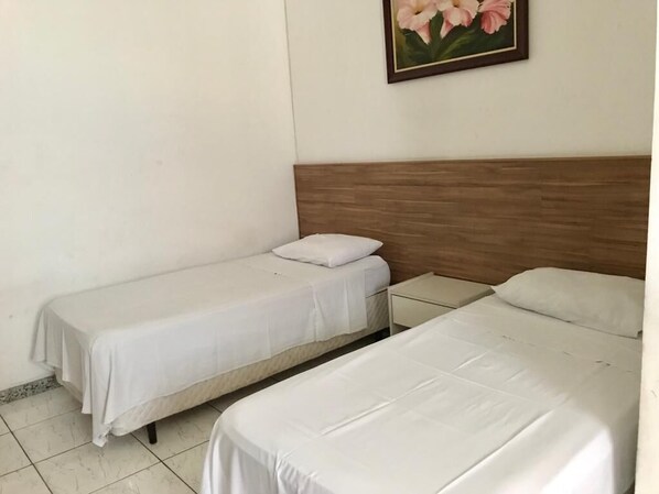 A hotel room with two single beds, a wooden headboard, a small bedside table, and a framed picture on the wall.