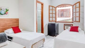 Quarto de hotel com duas camas de solteiro, uma mesinha, aquecedor e uma janela com persianas de madeira.